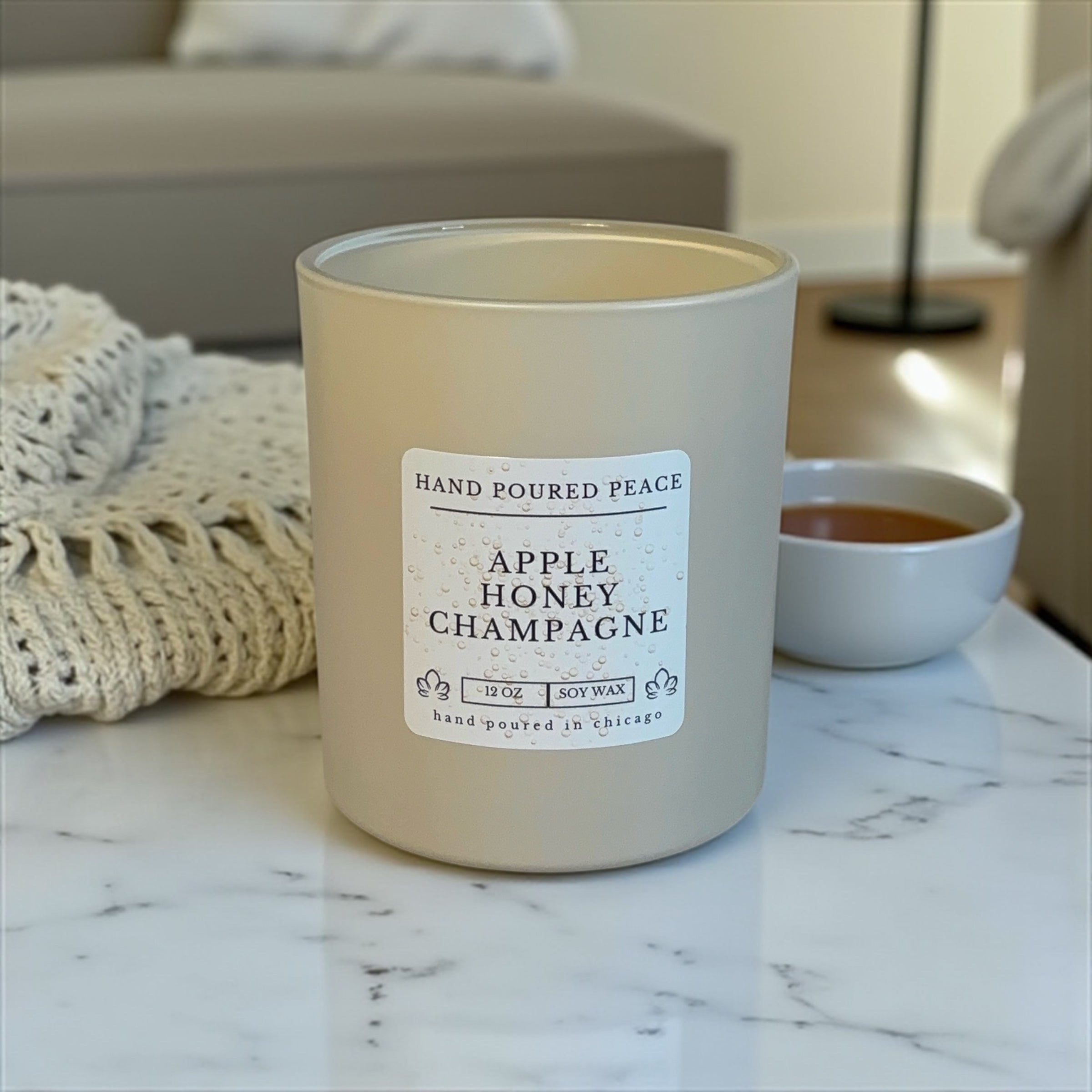 Candle labeled 'Apple Honey Champagne' on a marble surface with a blurred background
