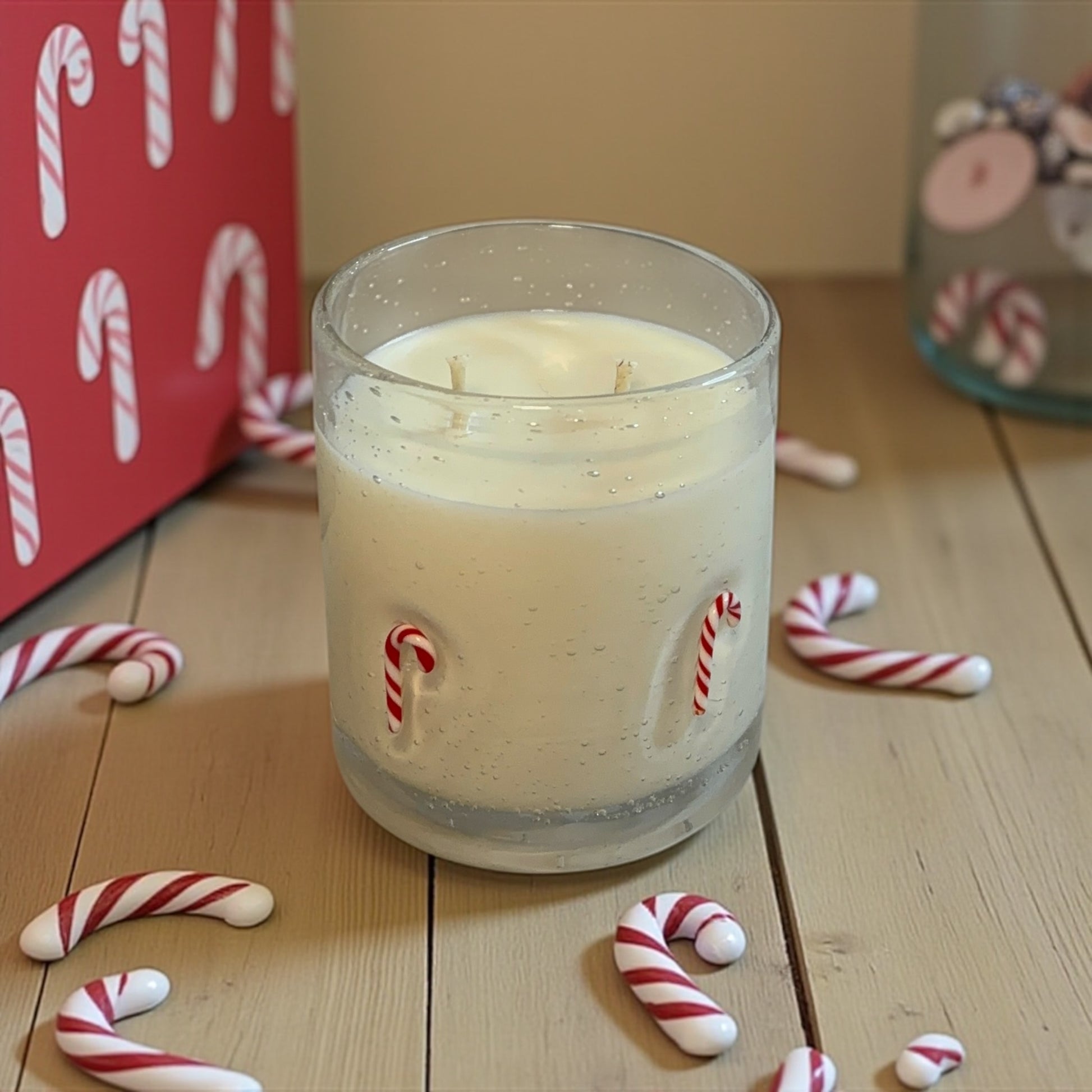 A GLASS CANDLE with candy canes on the vessel, a wooden surface