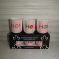 Three pink hand-poured candle jars with 'Ho Ho Ho!' holiday lettering designs, displayed on top of their black retail box labeled 'Hand Poured Peace Discovery Set'.