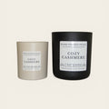 Two candles, one gray and one black, with 'Cozy Cashmere' labels on a white background.