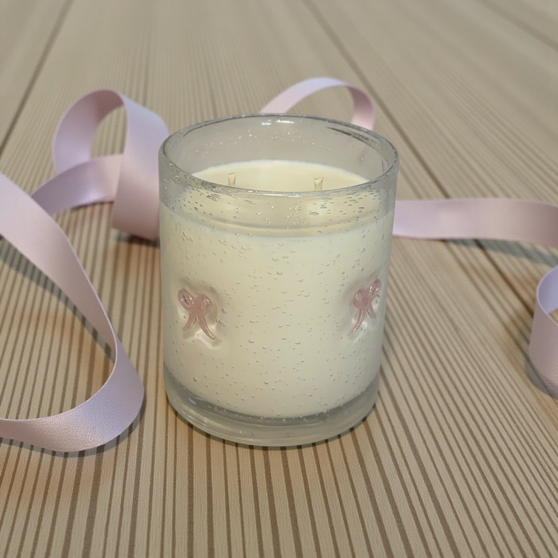 Candle in a glass jar with a pink ribbon on a wooden surface
