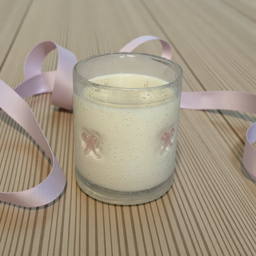 Candle in a glass jar with a pink ribbon on a wooden surface