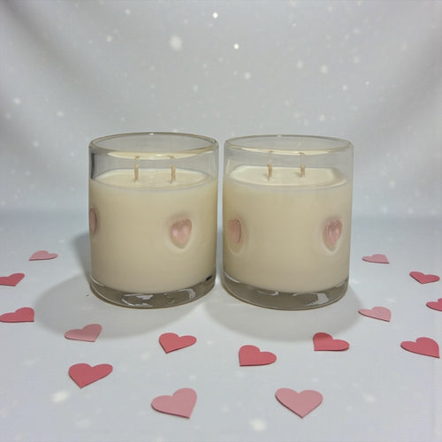 Two candles with pink heart shapes on a white background with scattered pink hearts.