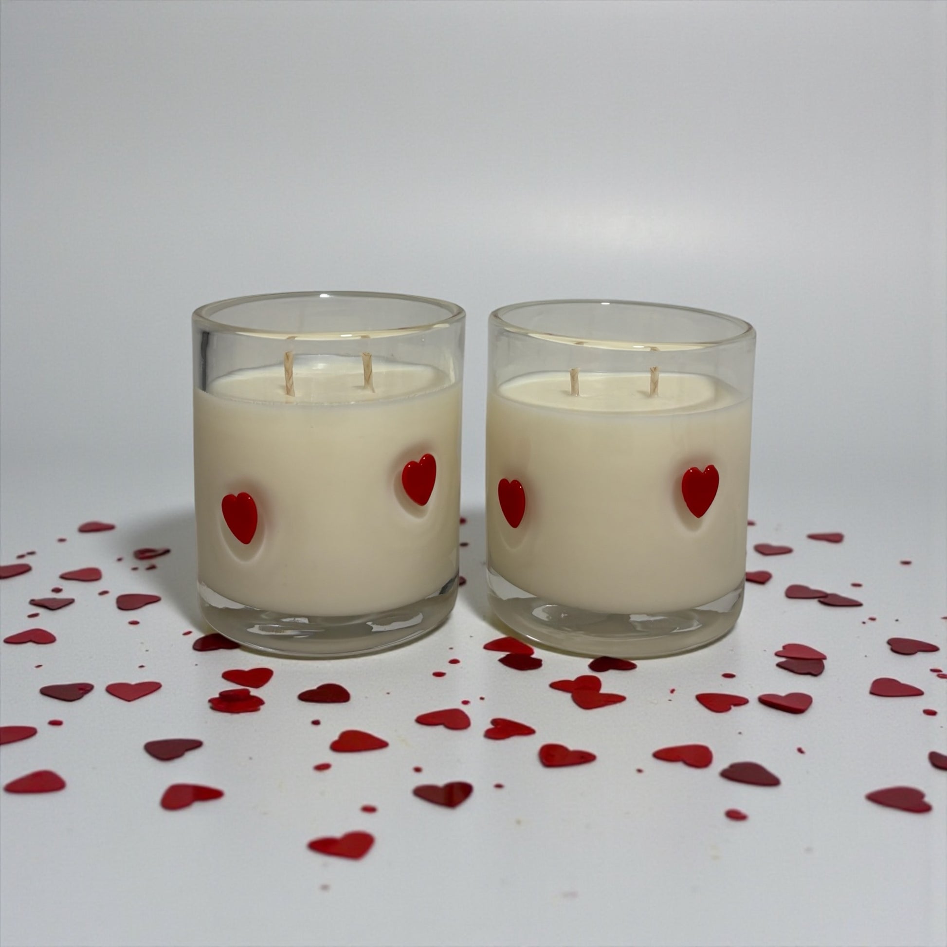 Two candles with red heart decorations on a white background with scattered red hearts.