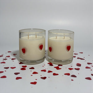 Two candles with red heart decorations on a white background with scattered red hearts.