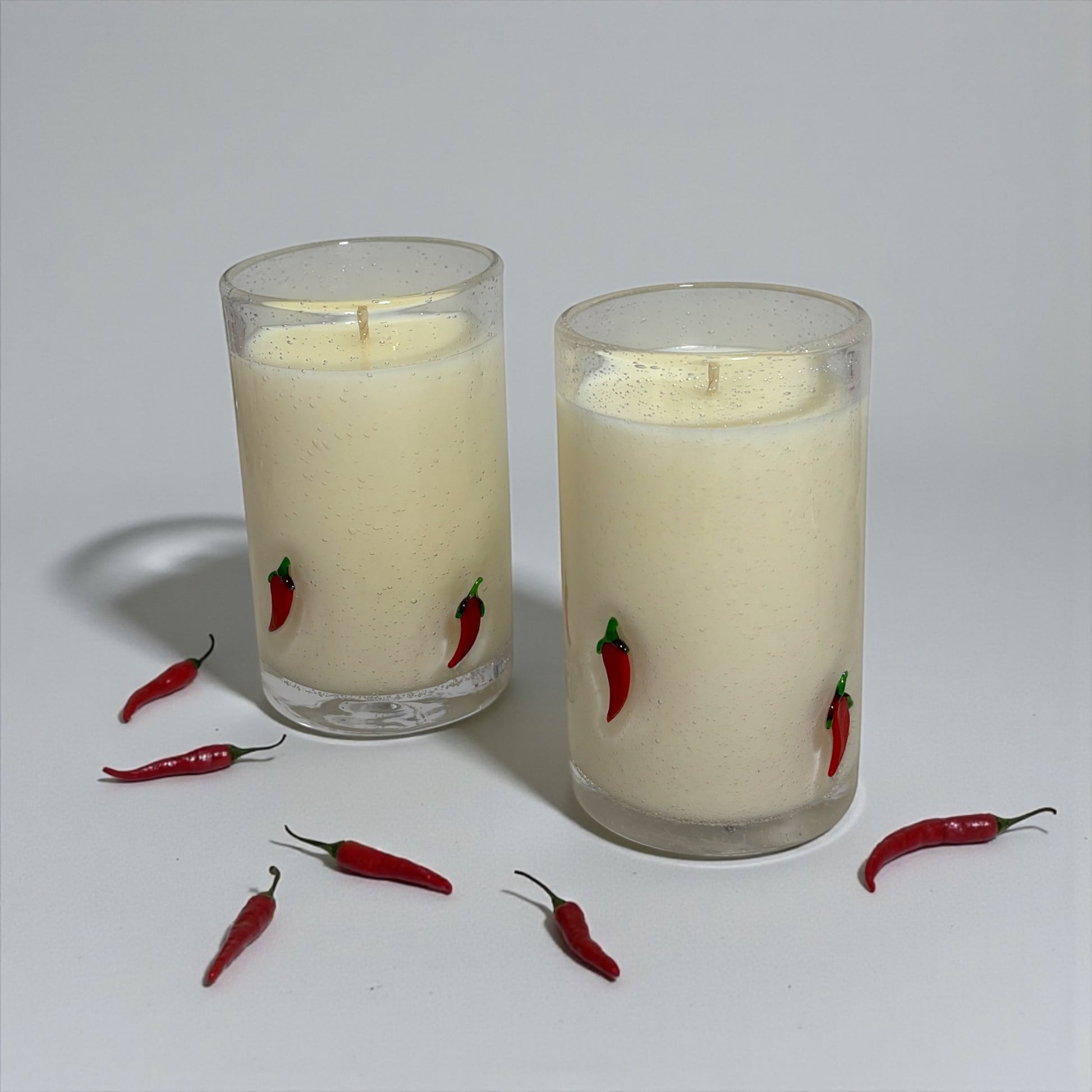 Two glass candles with red chili pepper designs on a white background