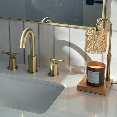 Bathroom sink with gold faucet and decorative lamp on a white countertop.